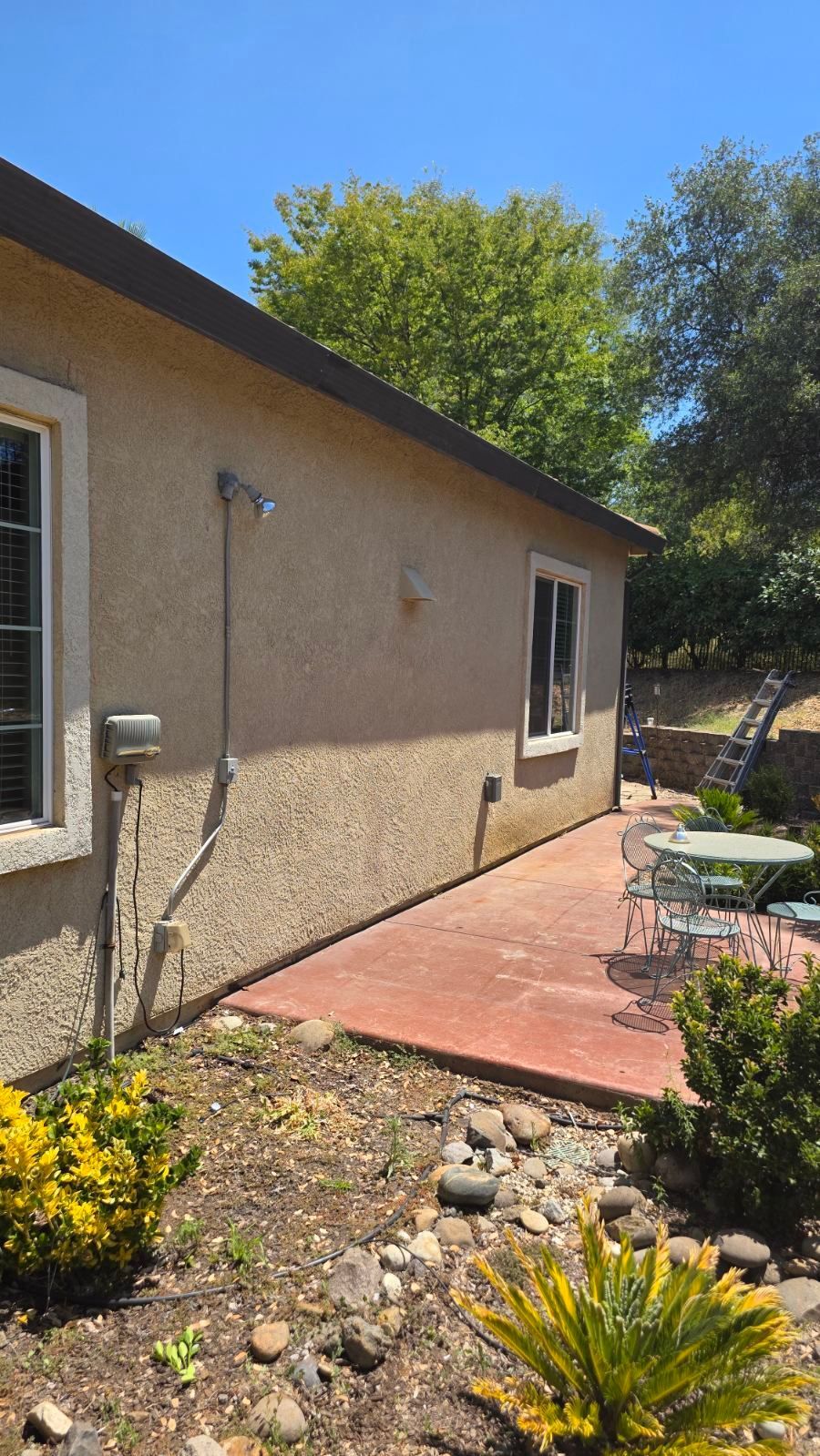 Tan stucco house with red patio. White window frames. Trees and a blue sky in the background.