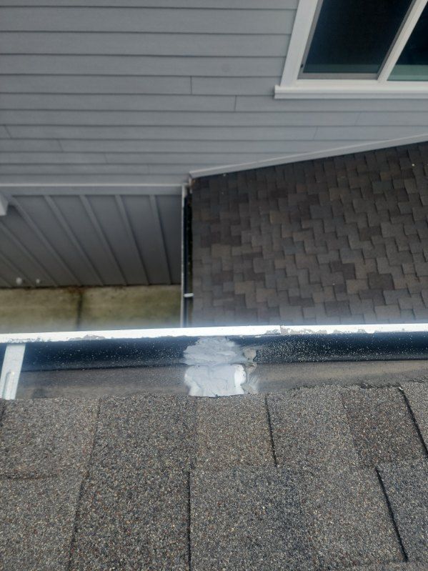 Gutter with sealant where roof meets wall, showing gray shingles and siding.
