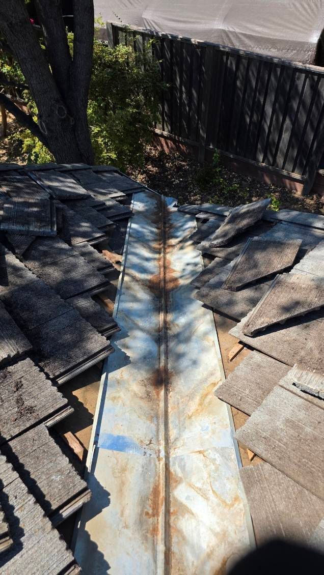 A metal roof valley with rusted sections surrounded by gray asphalt shingles.