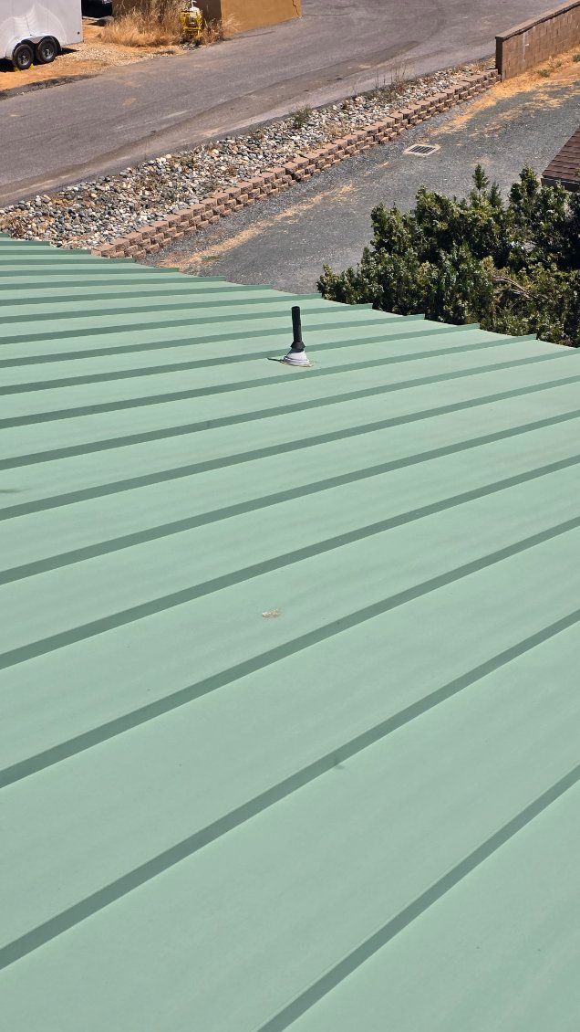 Green metal roof with a vent pipe; outdoors, sunny day.