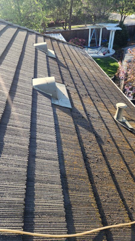 View of a weathered asphalt shingle roof with three vents; sunlight casts shadows.