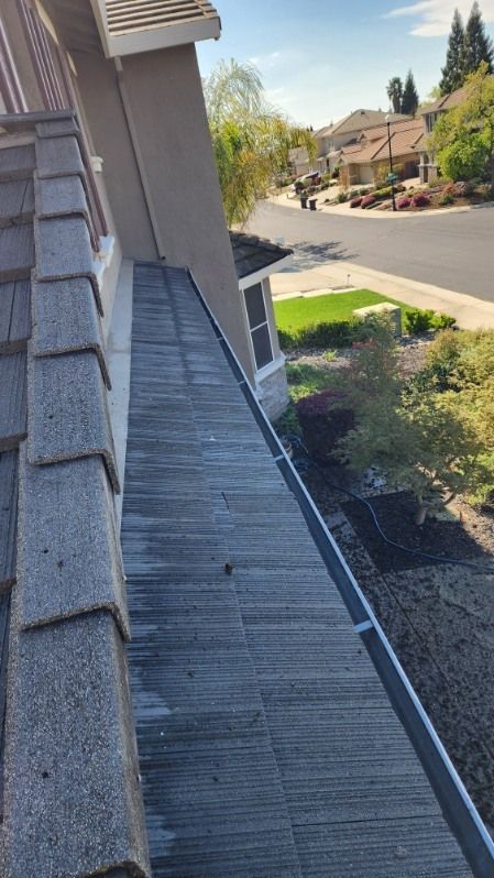 A side view of a house roof and gutter, with shingles on the left and a road in the distance.