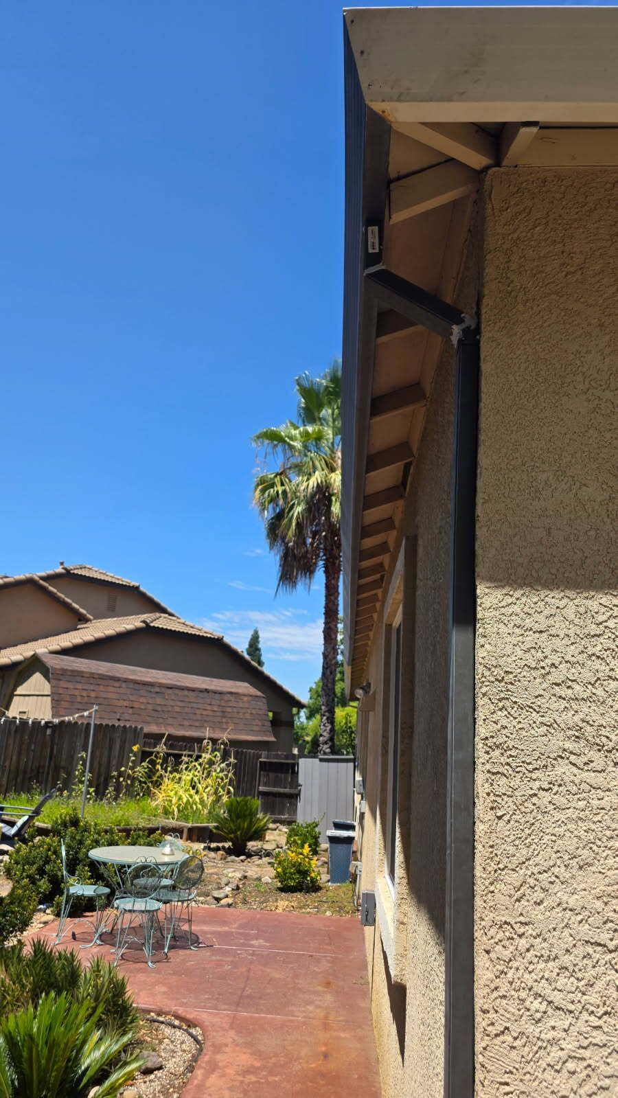 Side view of a beige house with black trim and a courtyard, clear blue sky overhead.
