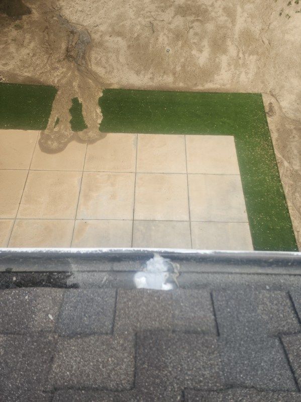 Overhead view of a tiled patio with faux green grass and a roof gutter.