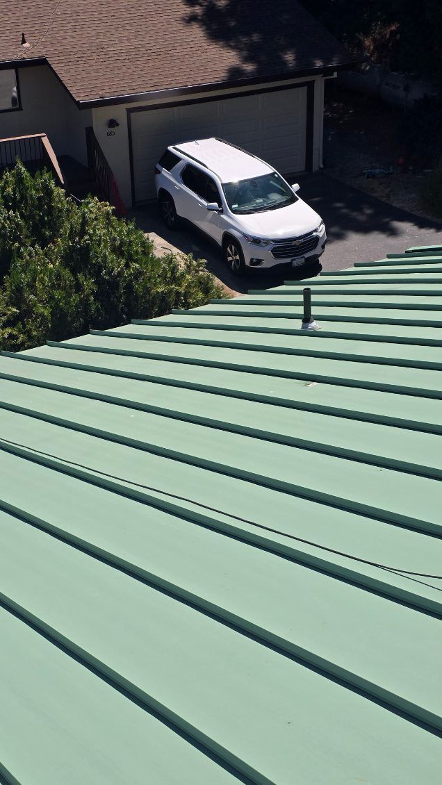 Green metal roof with a white SUV parked in front of a garage.