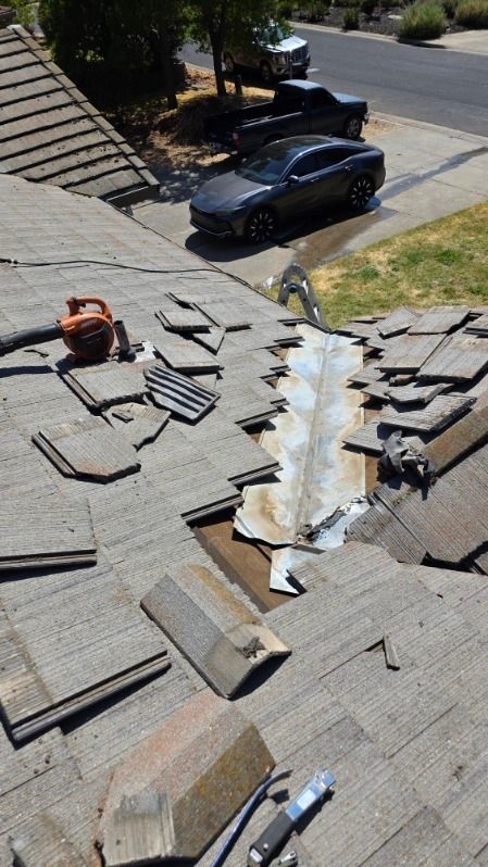 Damaged roof with missing tiles, exposing underlayment. A car sits in a driveway nearby.