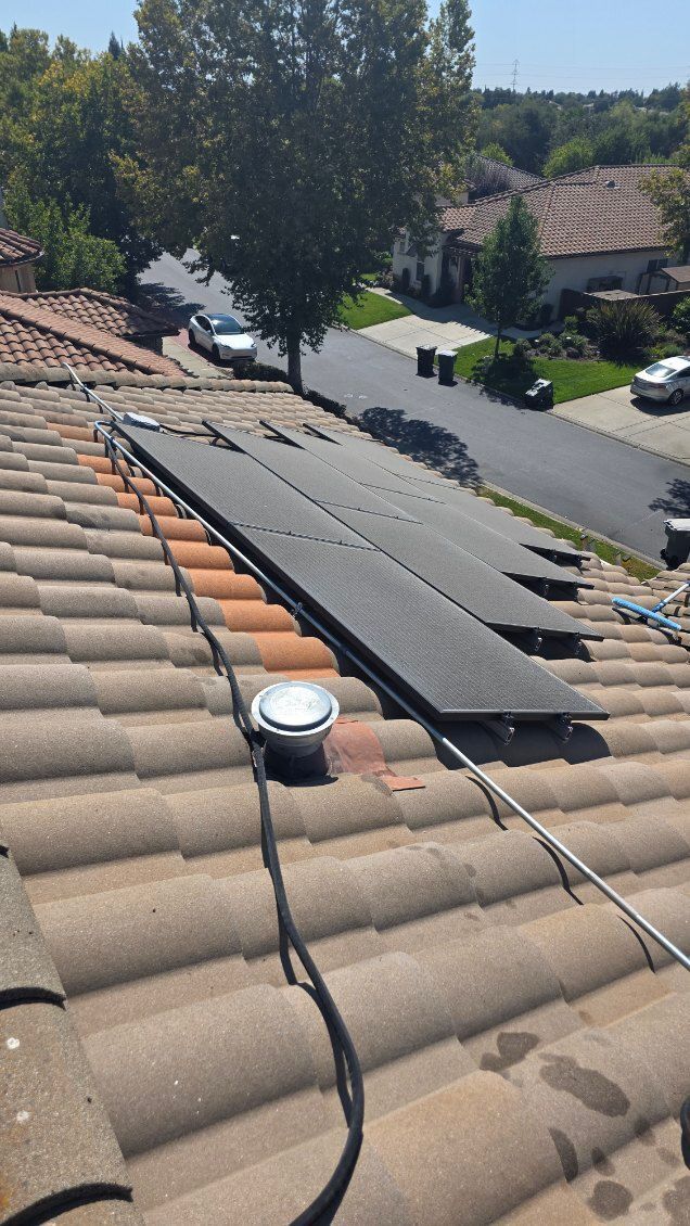 Solar panels on a tile roof, next to a pipe and conduit. Residential street in the background.
