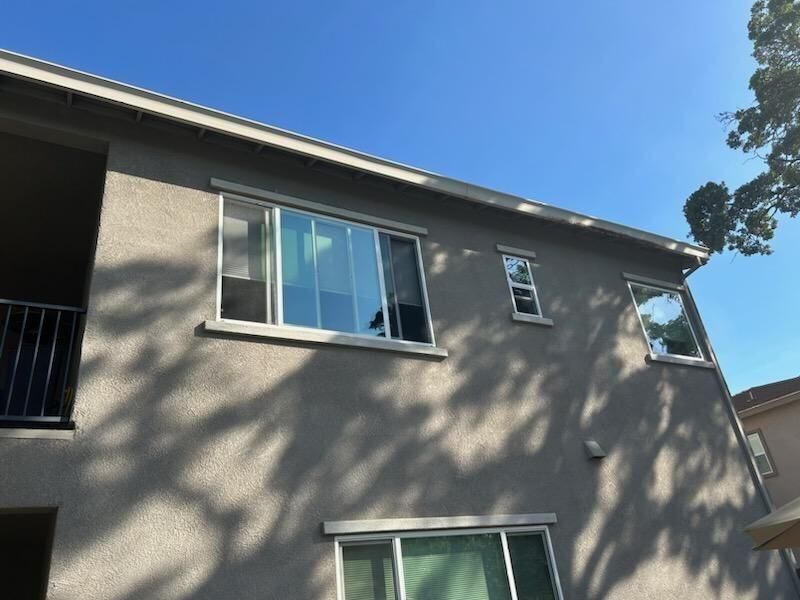 Gray stucco building with multiple windows against a bright blue sky.