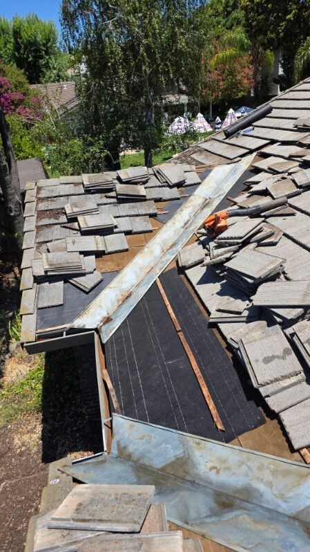 Roof with missing tiles and metal flashing. Exterior setting with trees and green foliage.
