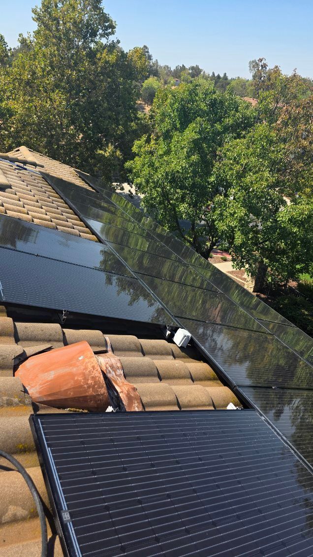 Solar panels installed on a tiled roof, with trees in the background under a blue sky.
