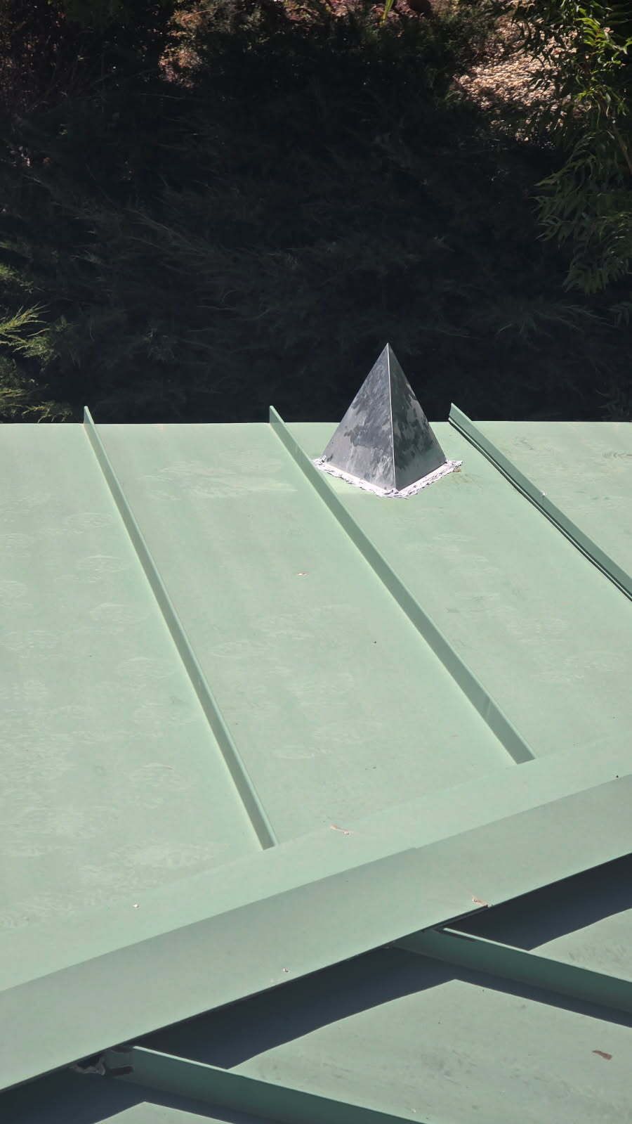 A pyramid-shaped metal roof vent on a green metal roof.