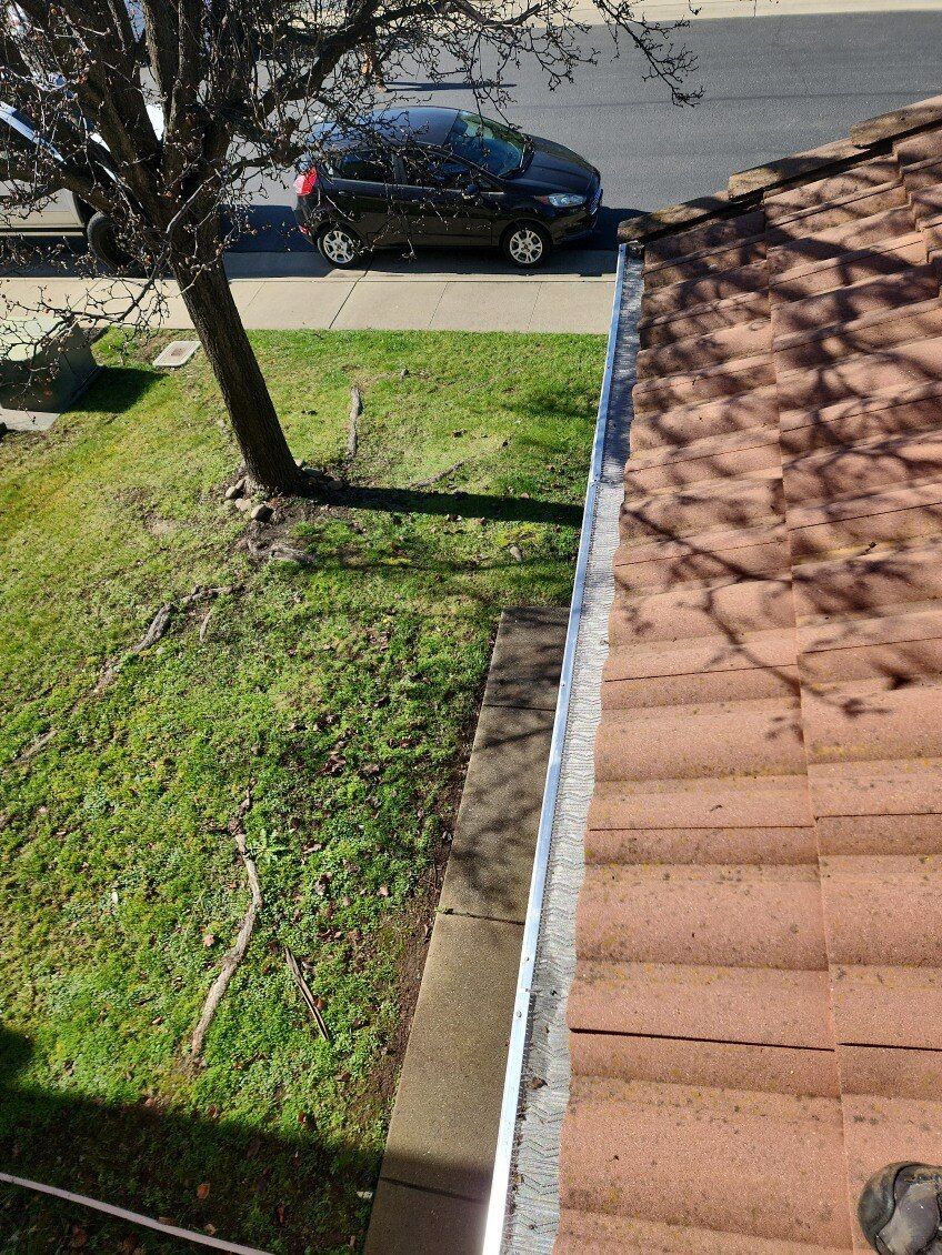 View from a rooftop of a grassy yard next to a sidewalk and a black car parked on the street.