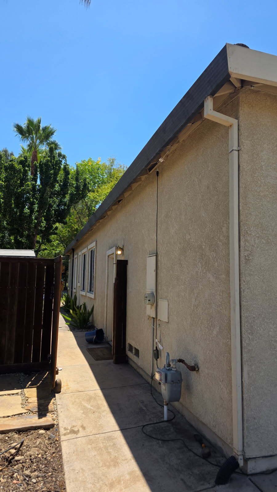 Side view of a beige stucco building with a pathway alongside. A gas meter and fence are visible.