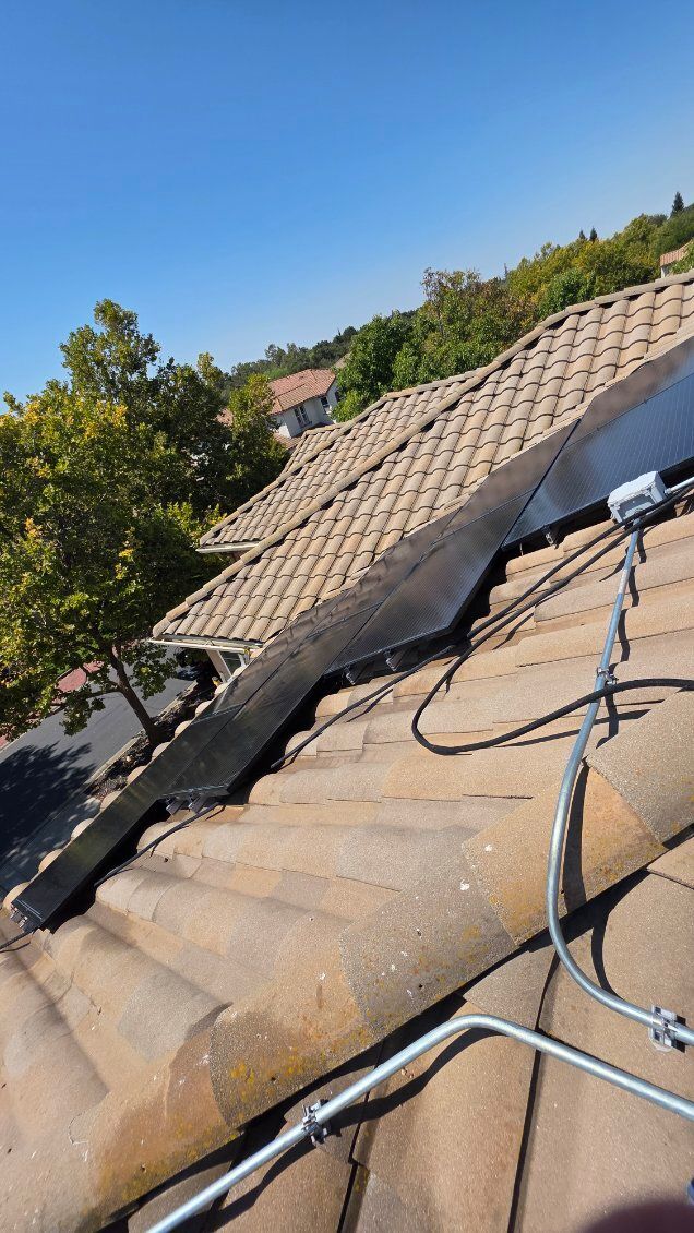 Solar panels on a tile roof with metal conduit, blue sky and trees in the background.
