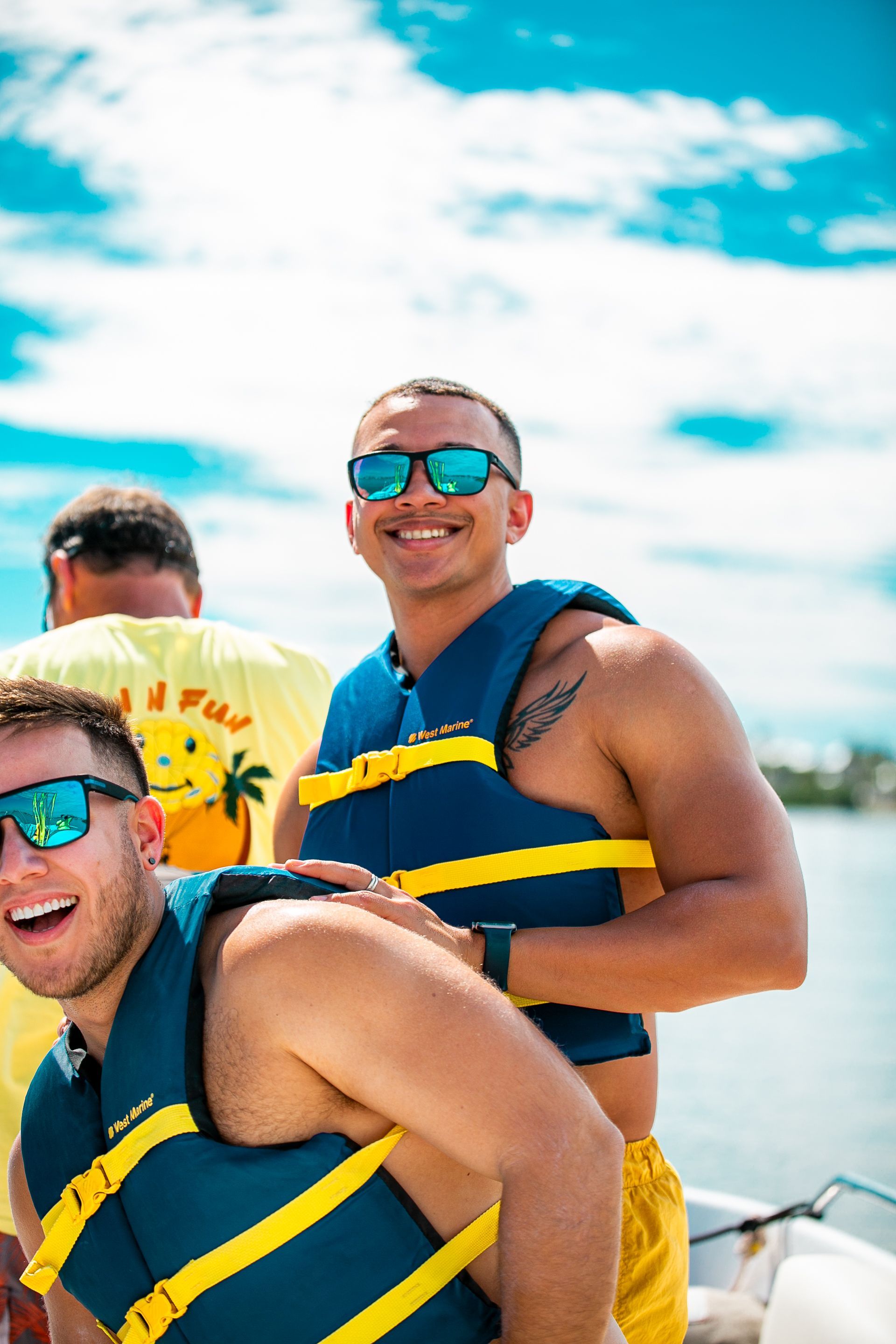 Three people in life jackets smile on a boat under a bright, blue sky.
