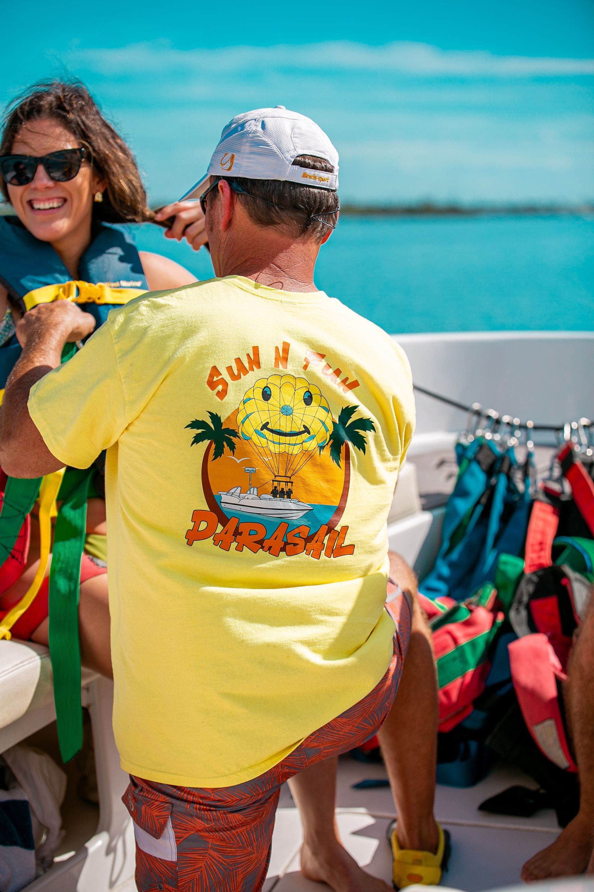 Man in yellow shirt helping woman with life vest on boat, sunny day.