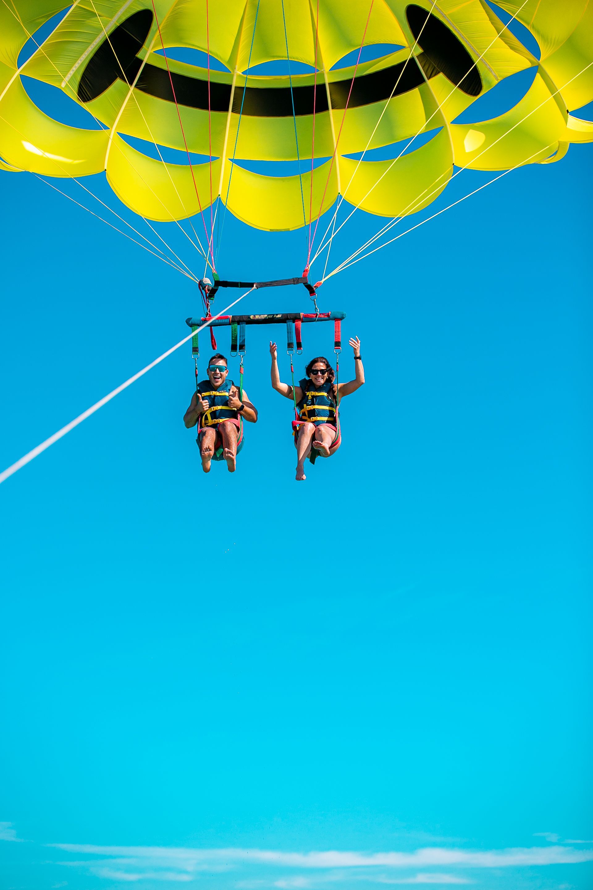 Two people parasailing in a bright blue sky, held by a yellow and black parachute.