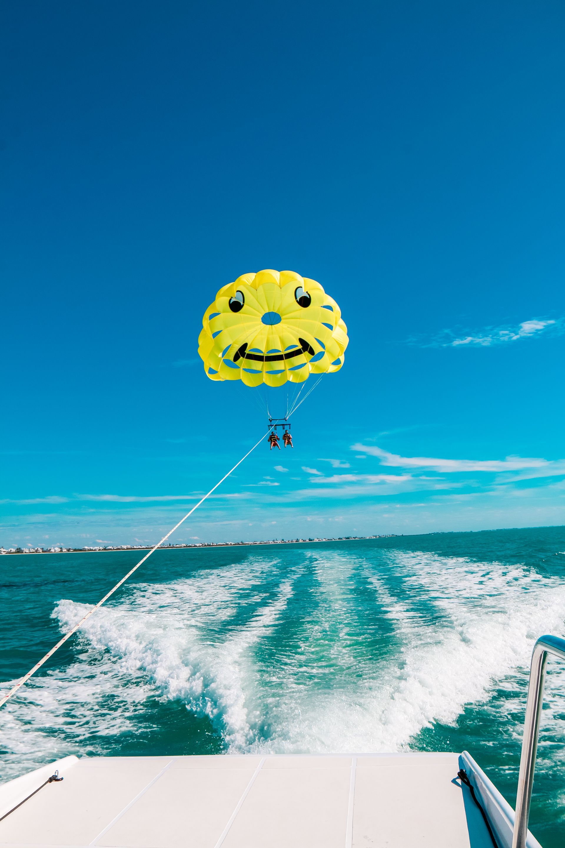Yellow parasail with smiling face pulled by a boat on the water; clear blue sky above.