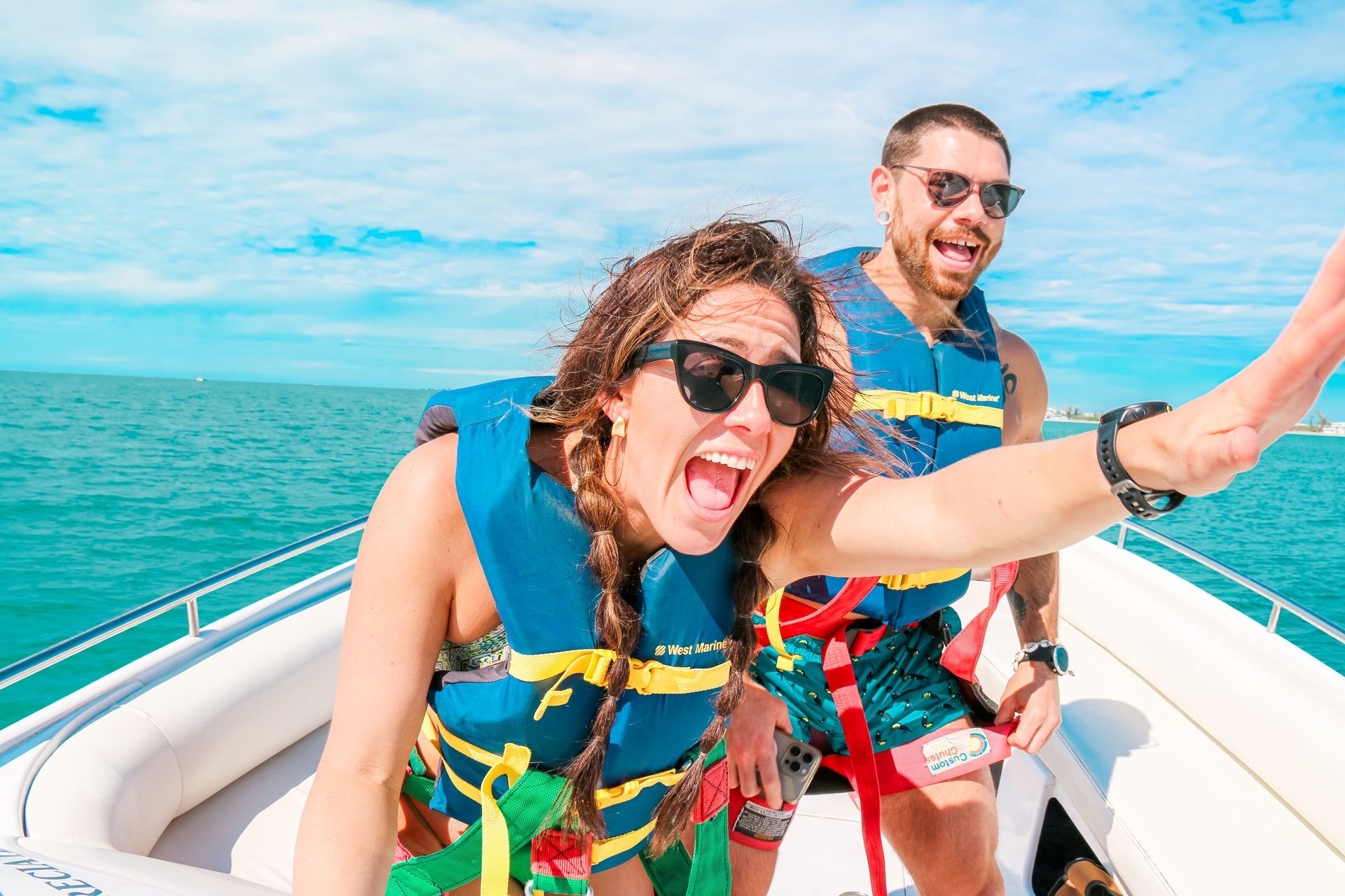 Woman and man in life vests on a boat, both smiling and looking excited on a sunny day.