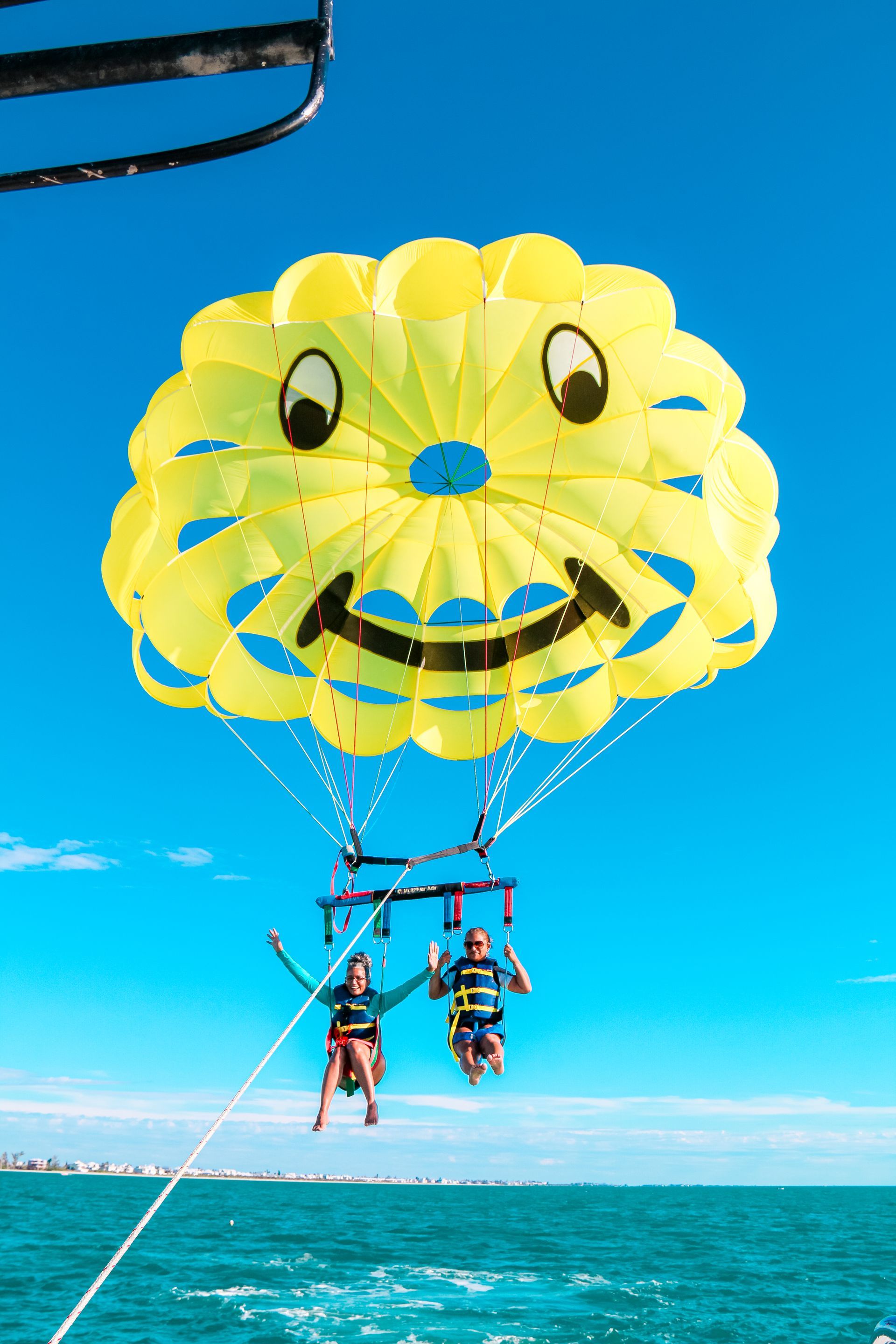 Two people parasailing with a yellow, smiling parachute over blue ocean.