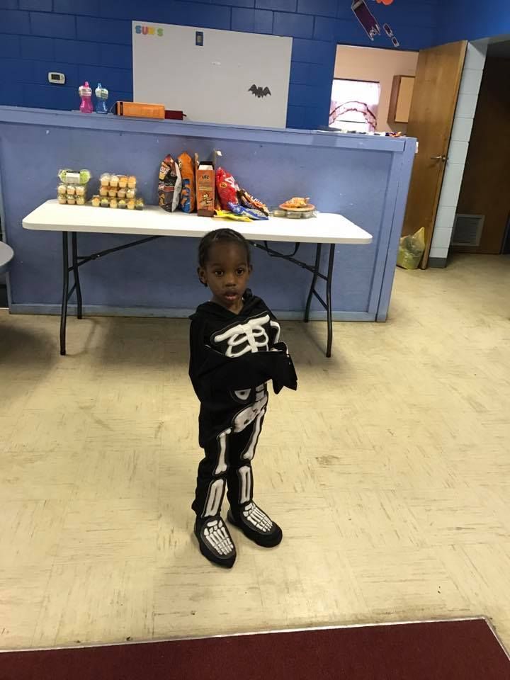 A little boy in a skeleton costume is standing in front of a table
