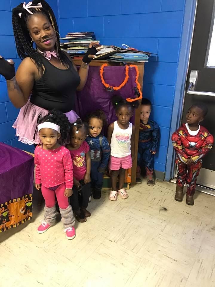 A woman is standing next to a group of children in a room.