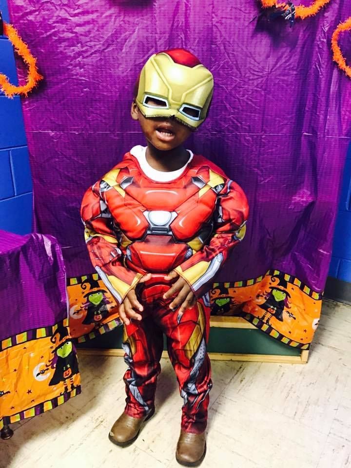 A young boy in an iron man costume is standing in front of a purple curtain.
