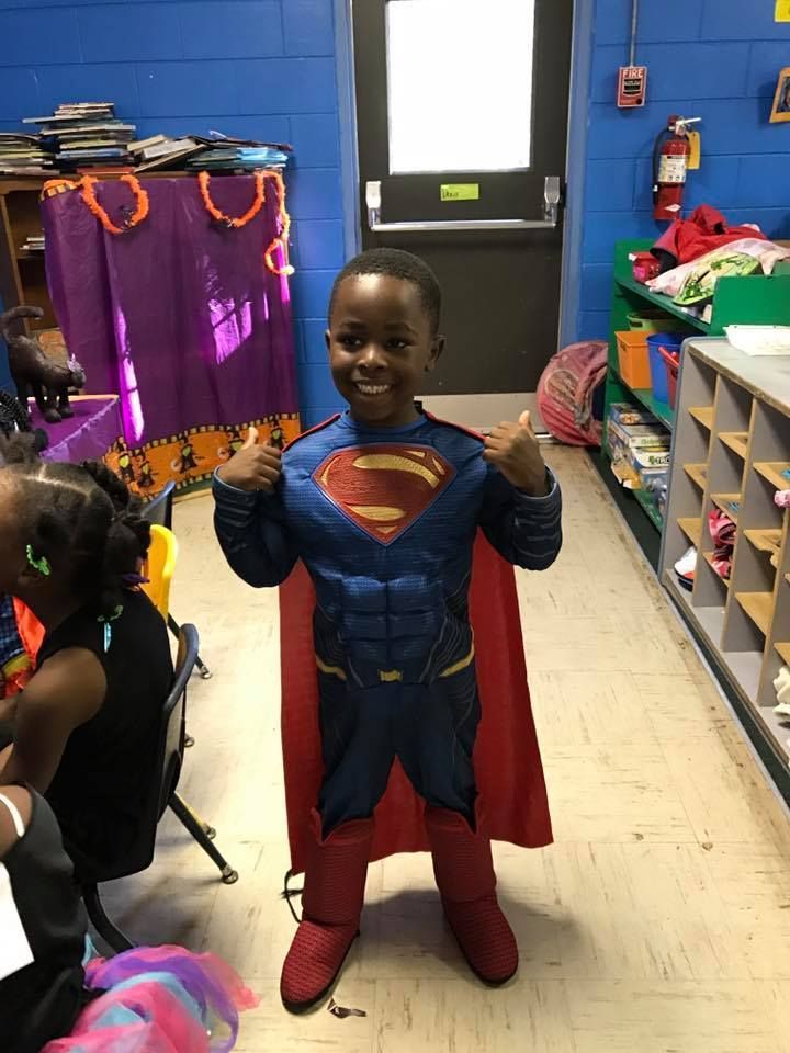 A young boy in a superman costume is giving a thumbs up.