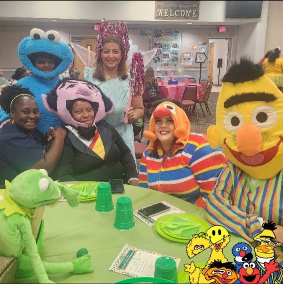 A group of sesame street characters are posing for a picture at a table