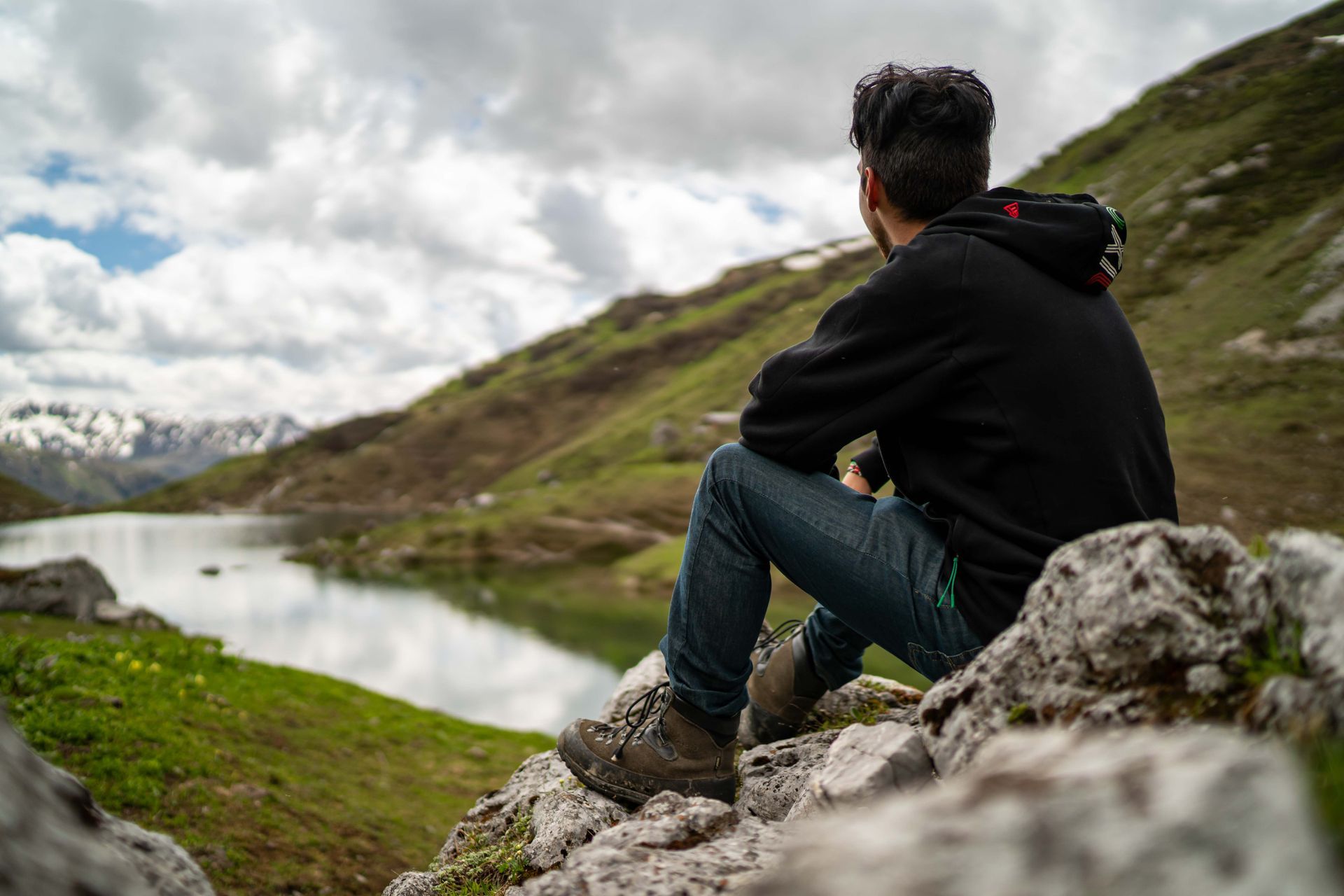 Ein Mann sitzt auf einem Felsen und blickt auf einen See.