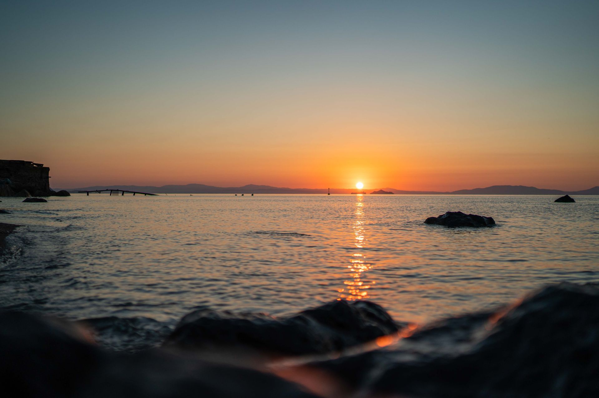 Eine Person liegt am Strand und beobachtet den Sonnenuntergang über dem Meer.