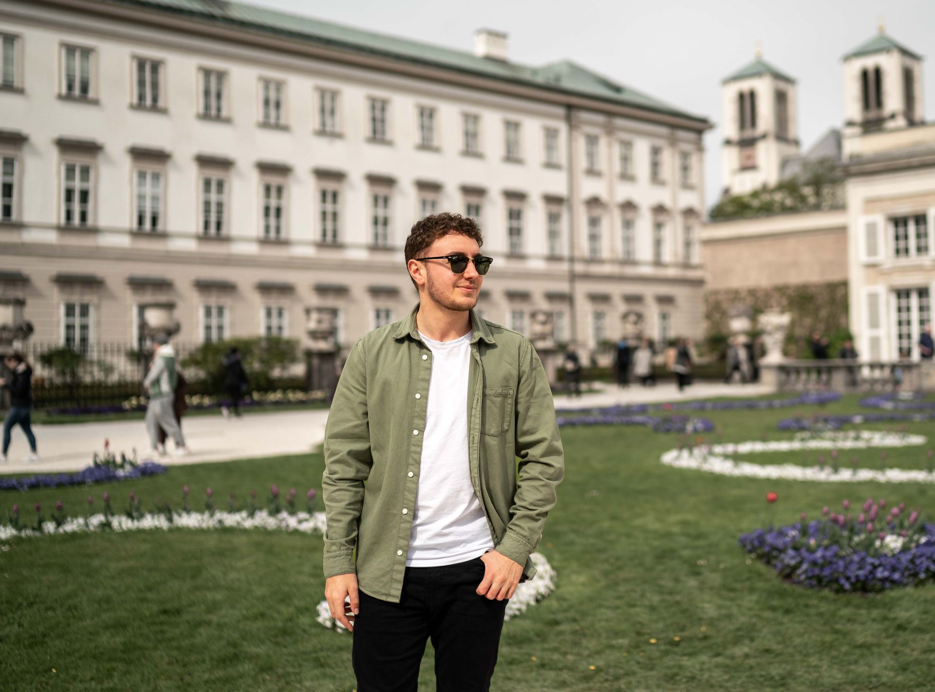 Ein Mann mit Sonnenbrille und grünem Hemd steht vor einem Gebäude.