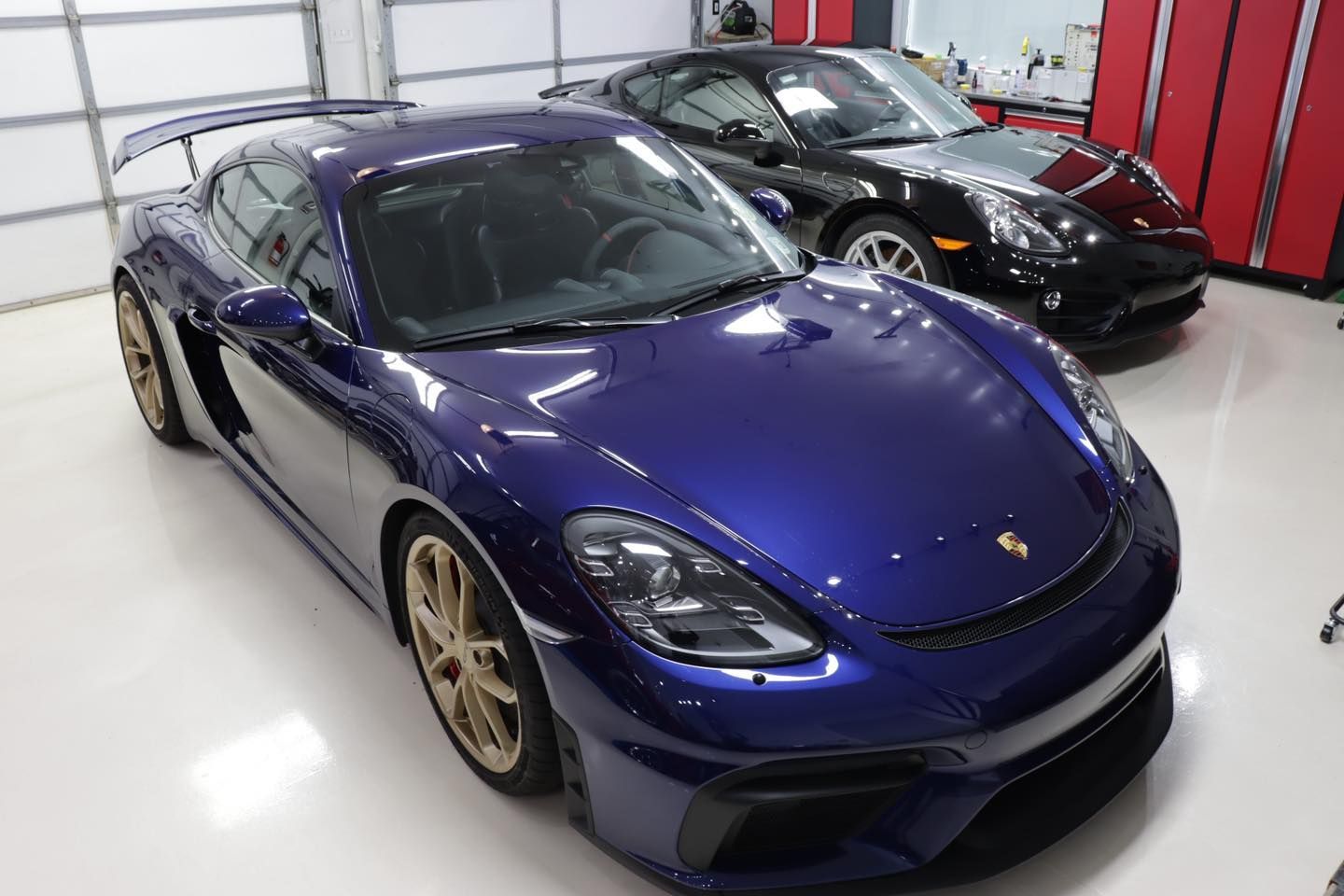 A blue Porsche Cayman GT4 and black Porsche parked in a garage.