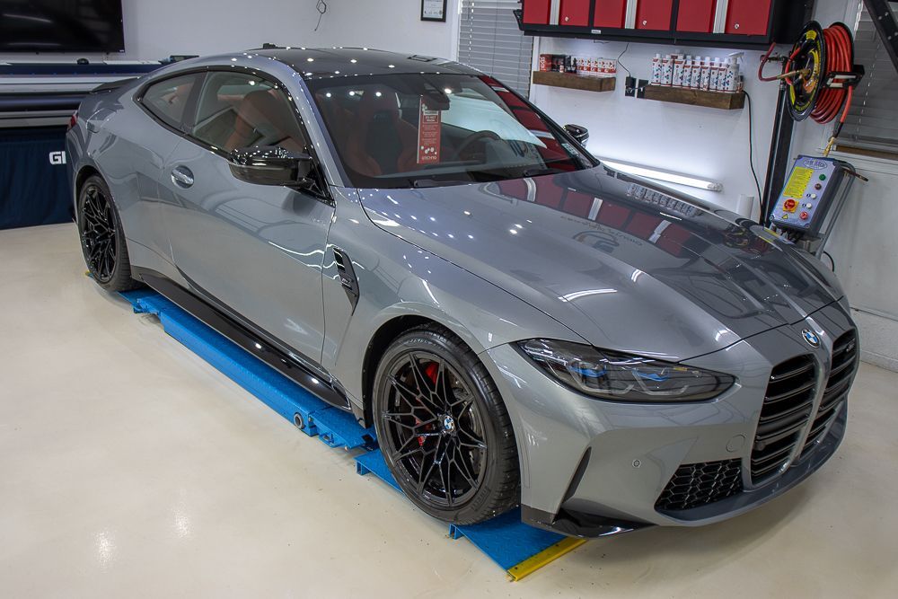 Gray BMW M4 coupe parked inside a garage. Black wheels and accents, red interior visible, shiny surface.