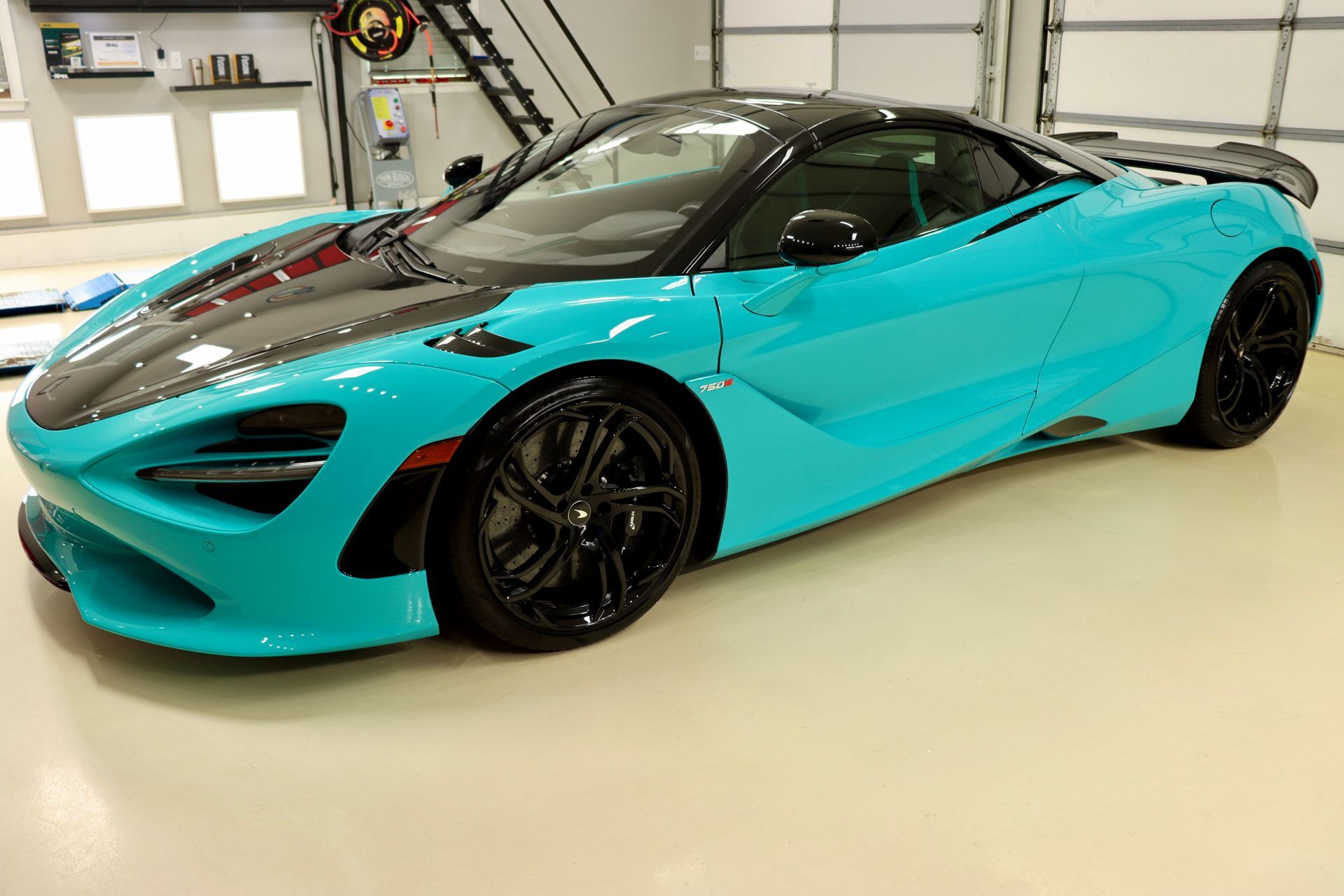 Bright turquoise McLaren sports car with a black roof and black wheels parked indoors.