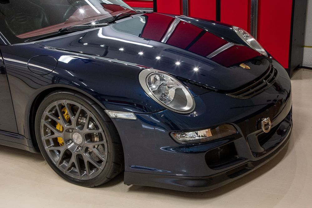 Dark blue Porsche sports car, parked, front view. Gray wheels, yellow brake calipers.