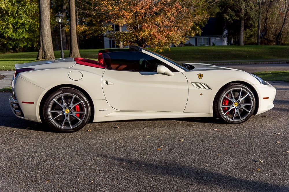 White Ferrari convertible parked on a paved road with a red interior.