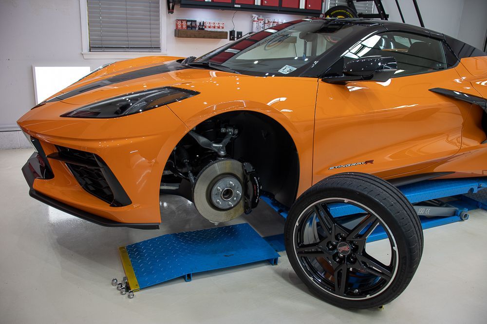 Orange Corvette on a lift with a removed wheel in a garage.