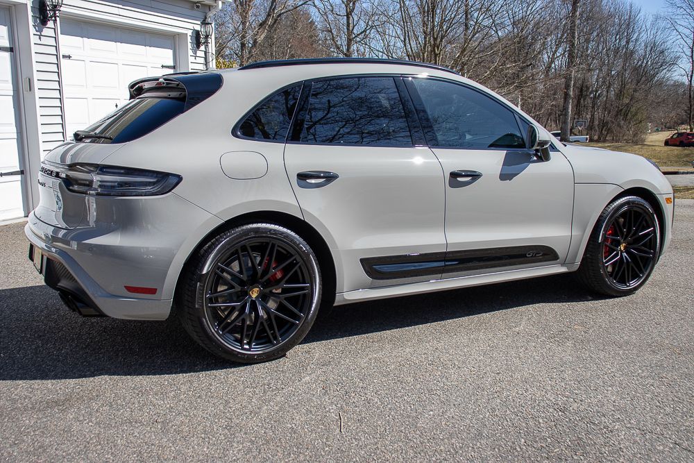 Gray Porsche Macan SUV with black wheels parked outside a garage on a sunny day.