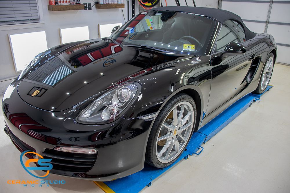 Black Porsche Boxster convertible in a garage, shiny paint.