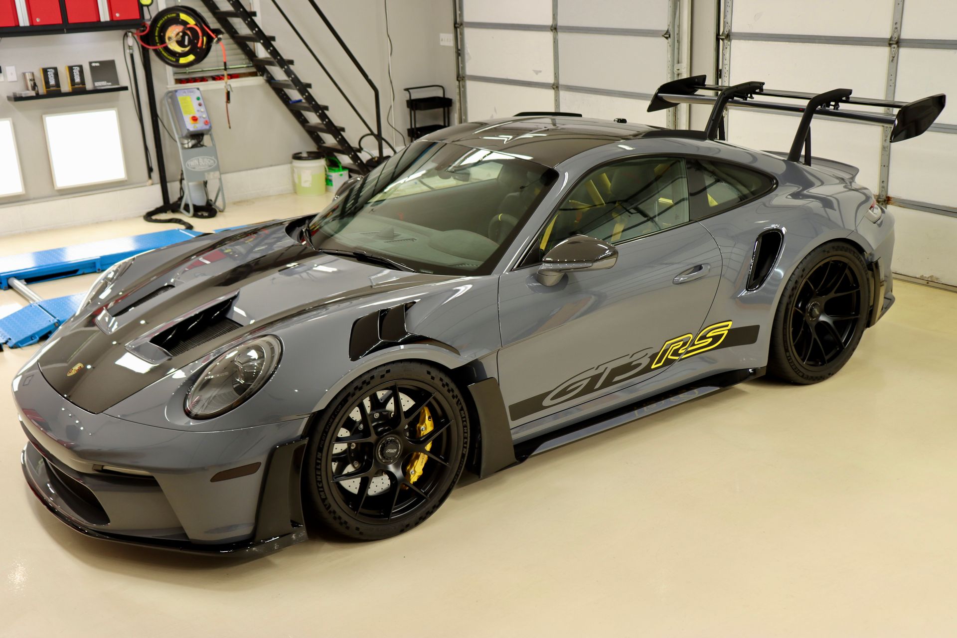 Gray Porsche GT3 RS sports car in a garage, black wheels, yellow brake calipers, and a large rear wing.
