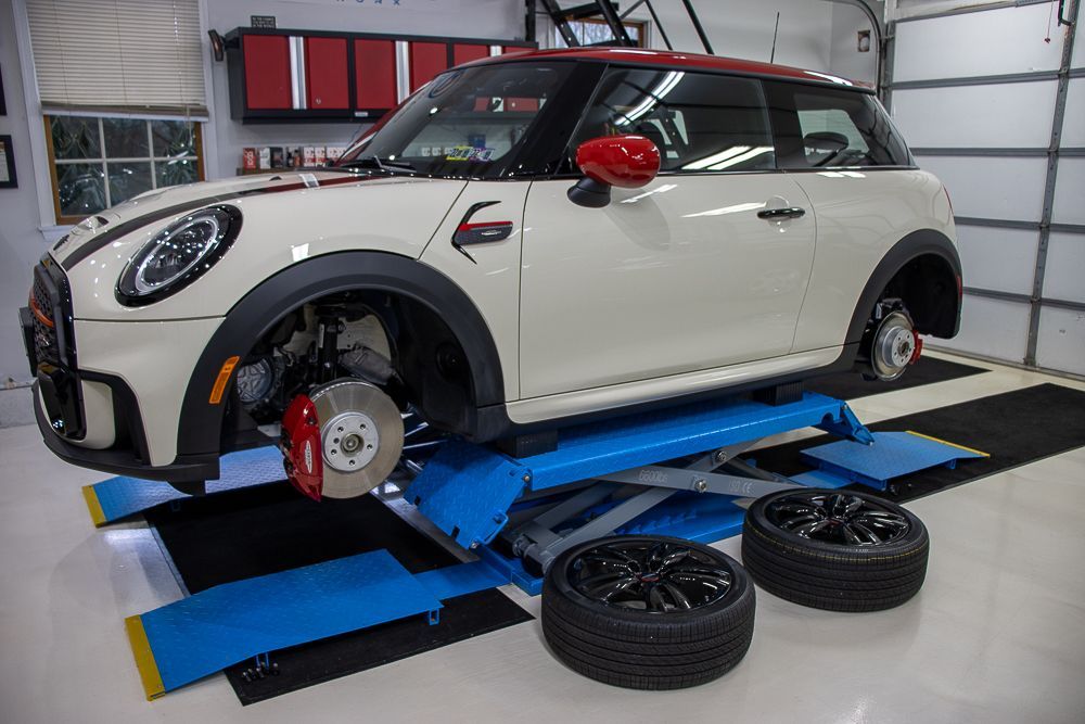 White and red Mini Cooper on a blue car lift, with two black tires in front of it, in a garage.