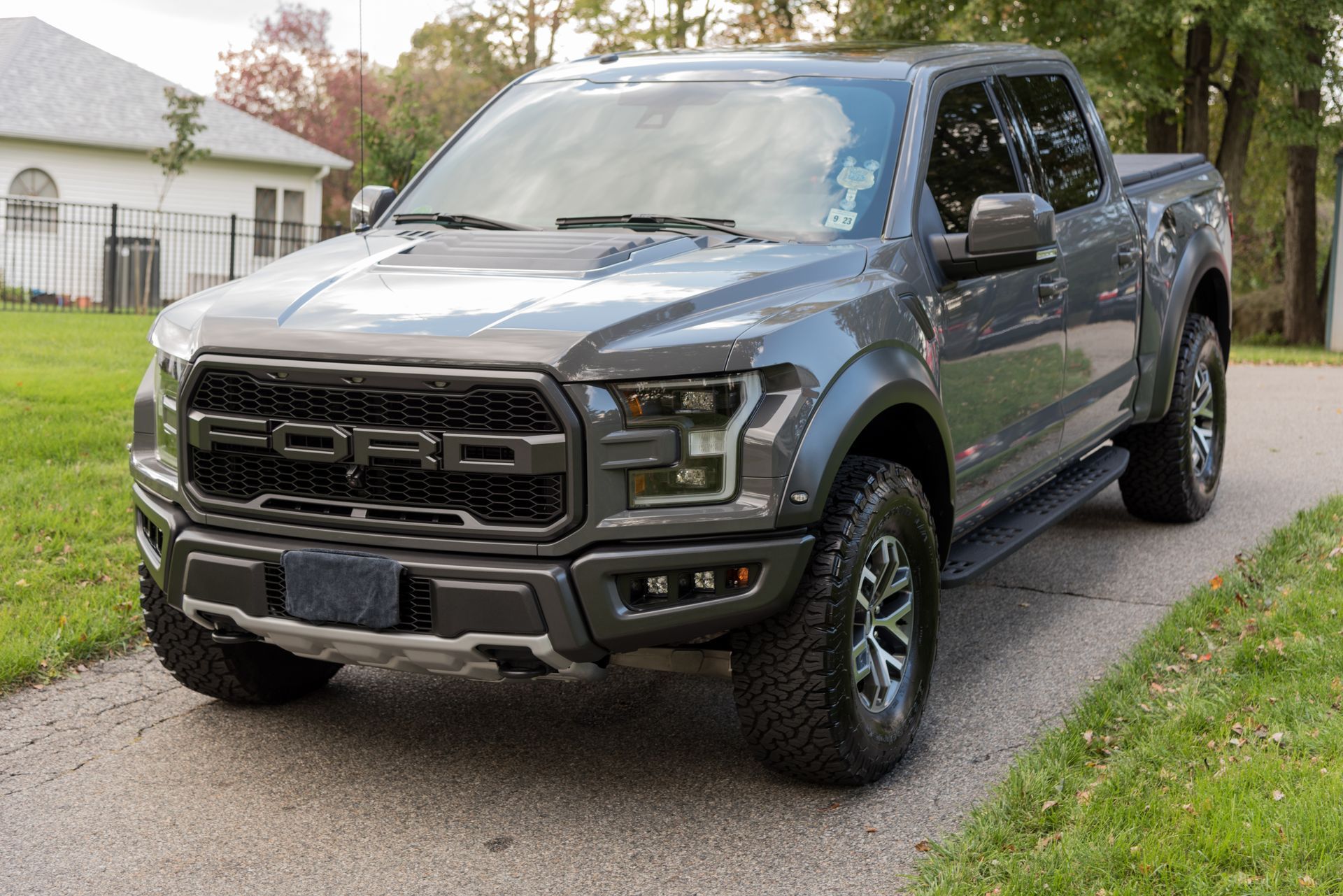 Gray Ford Raptor pickup truck parked on a driveway next to grass.