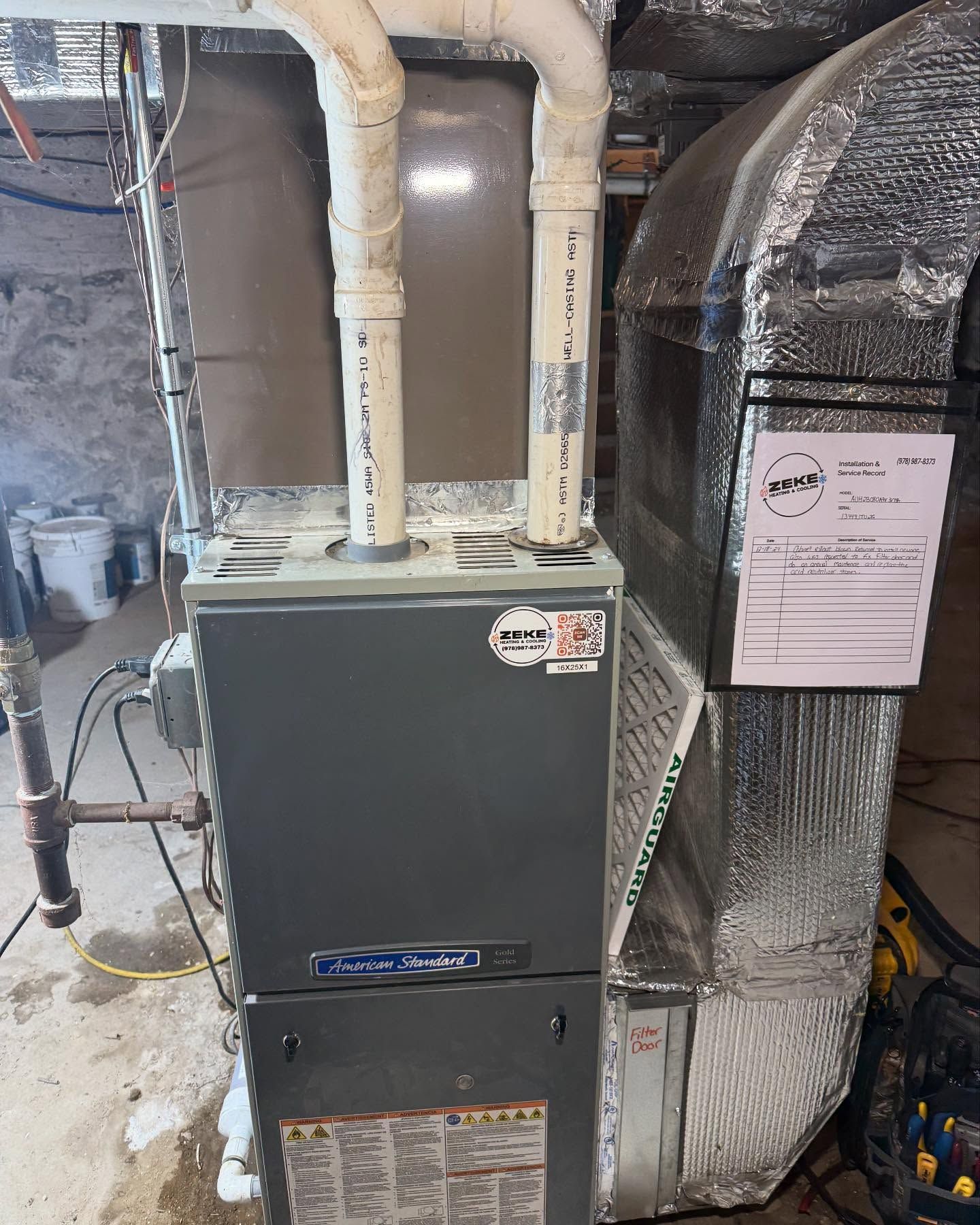 An air conditioner is sitting in a basement next to a duct.