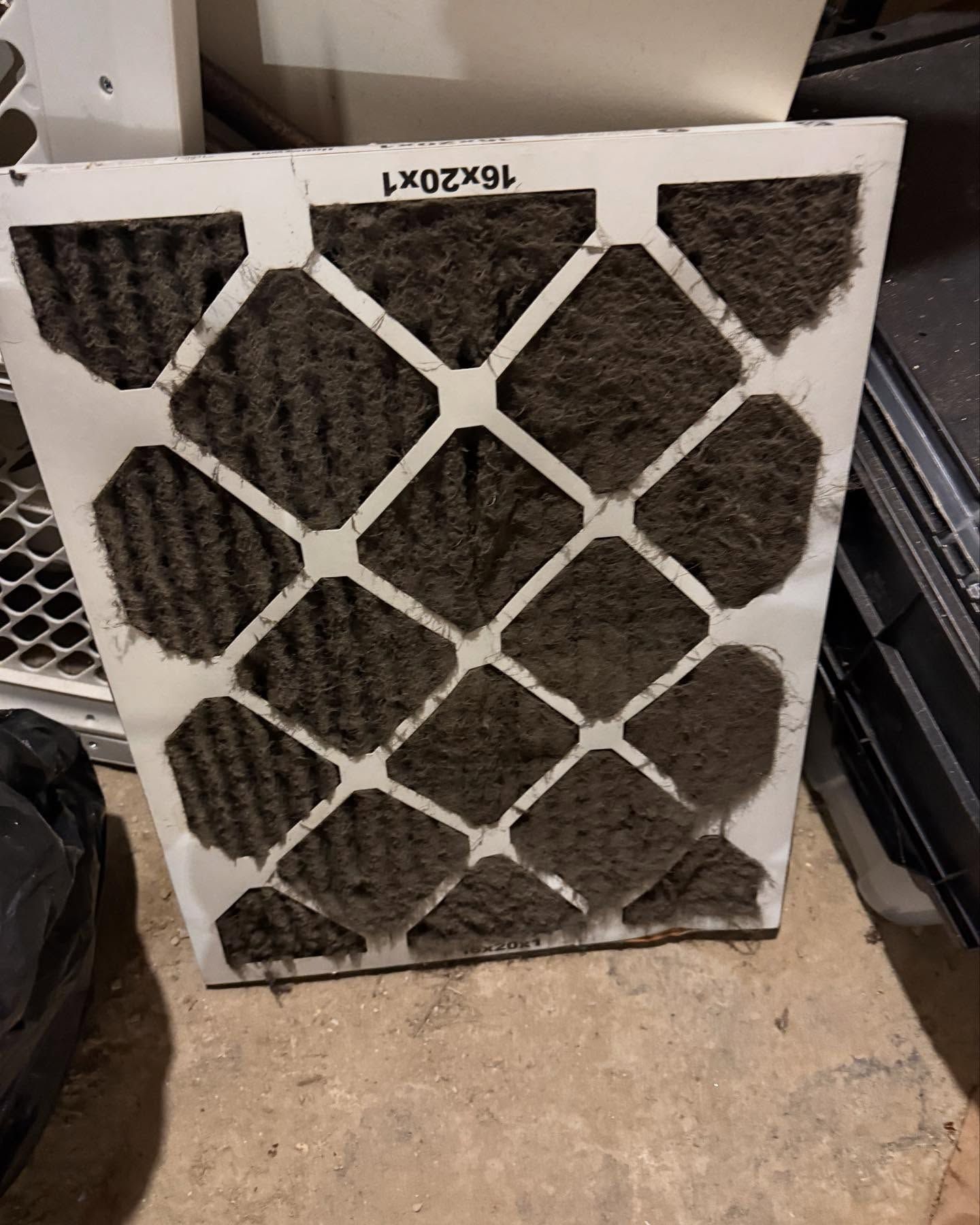 A dirty air filter is sitting on the floor next to a fan.