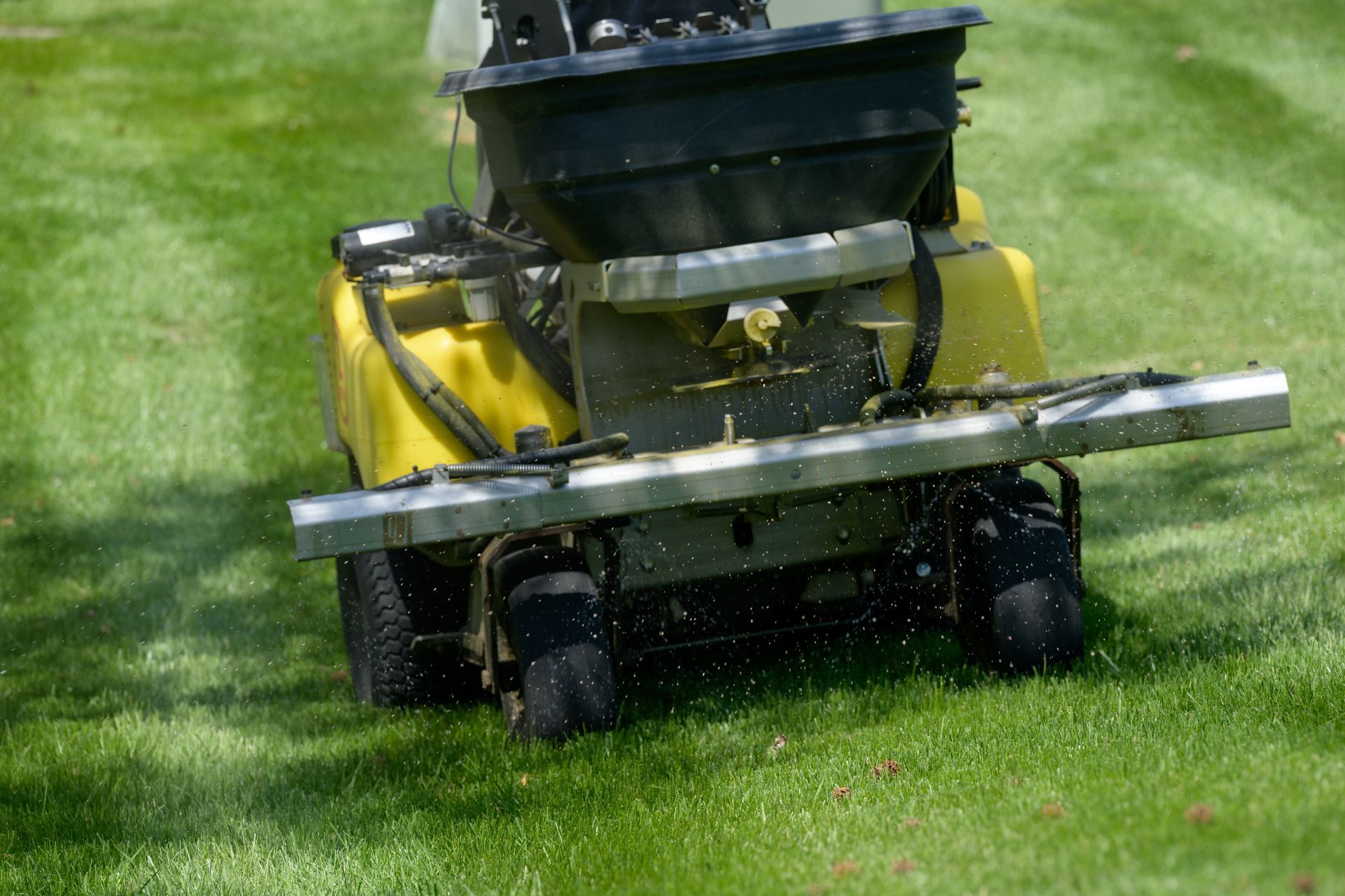 A yellow machine spreads fertilizer across a green, manicured lawn.