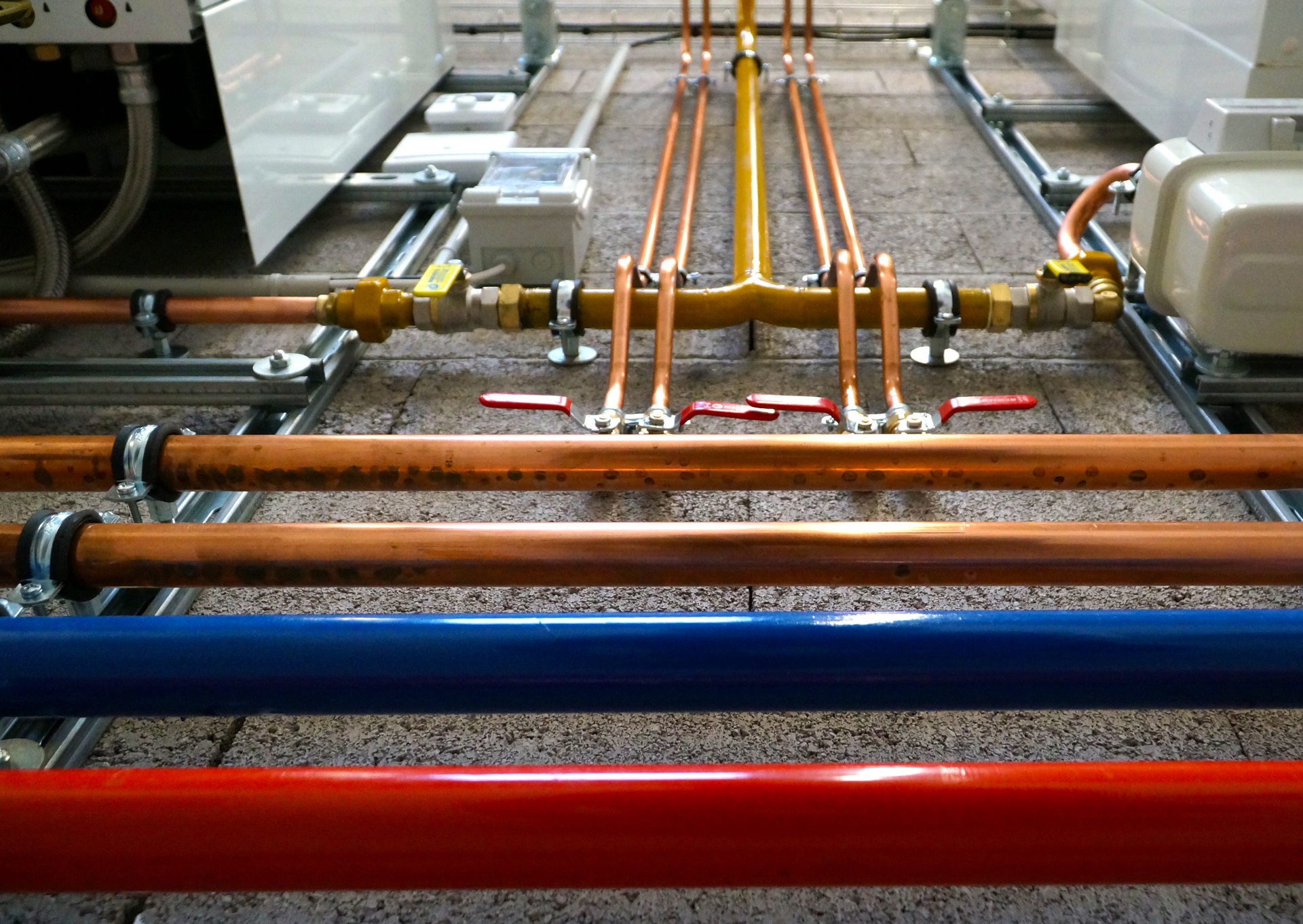 Plumbing system with copper, blue, and red pipes, valves, and brackets in a utility room.