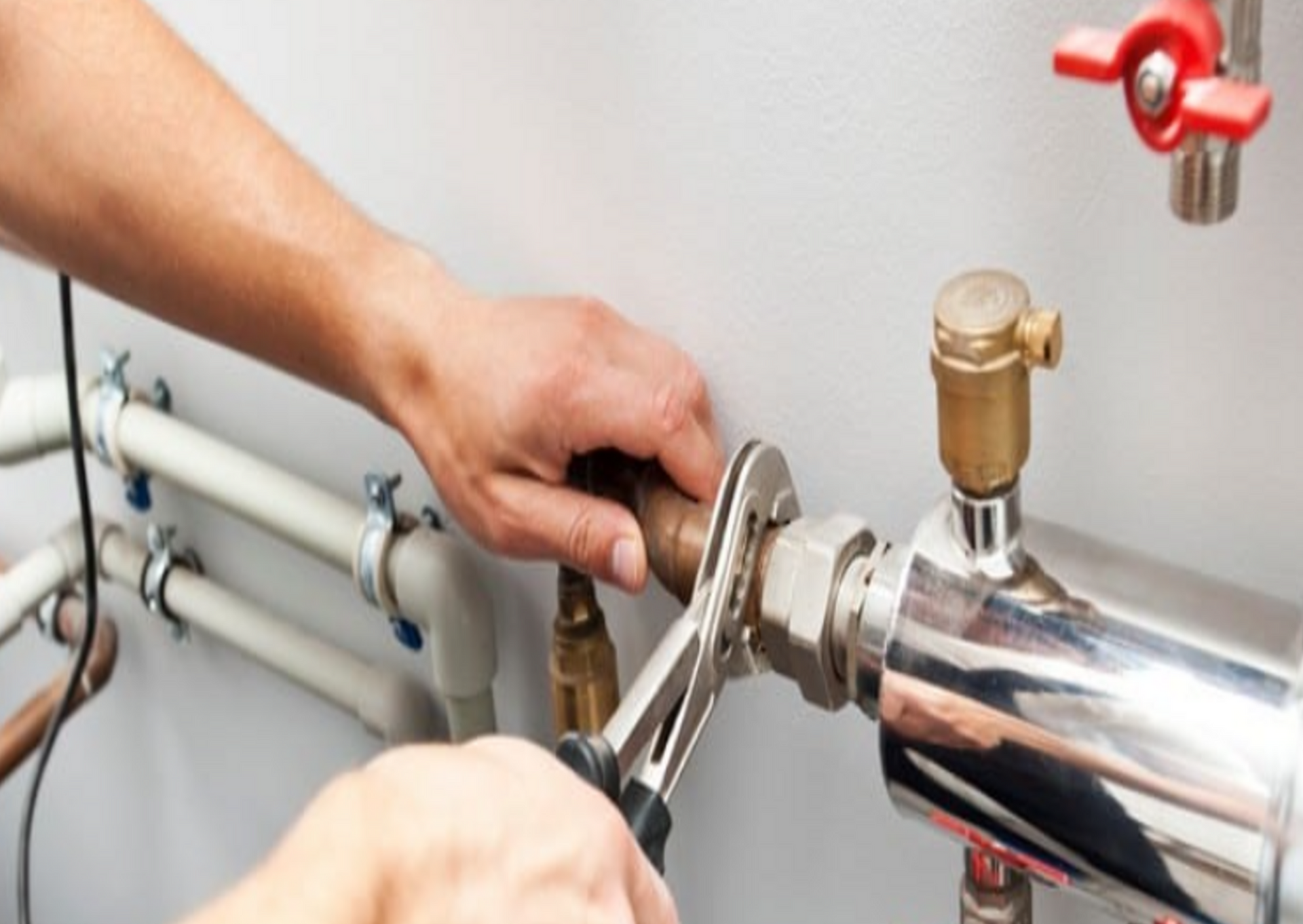 Plumber using a wrench to tighten a pipe connection near a silver tank.