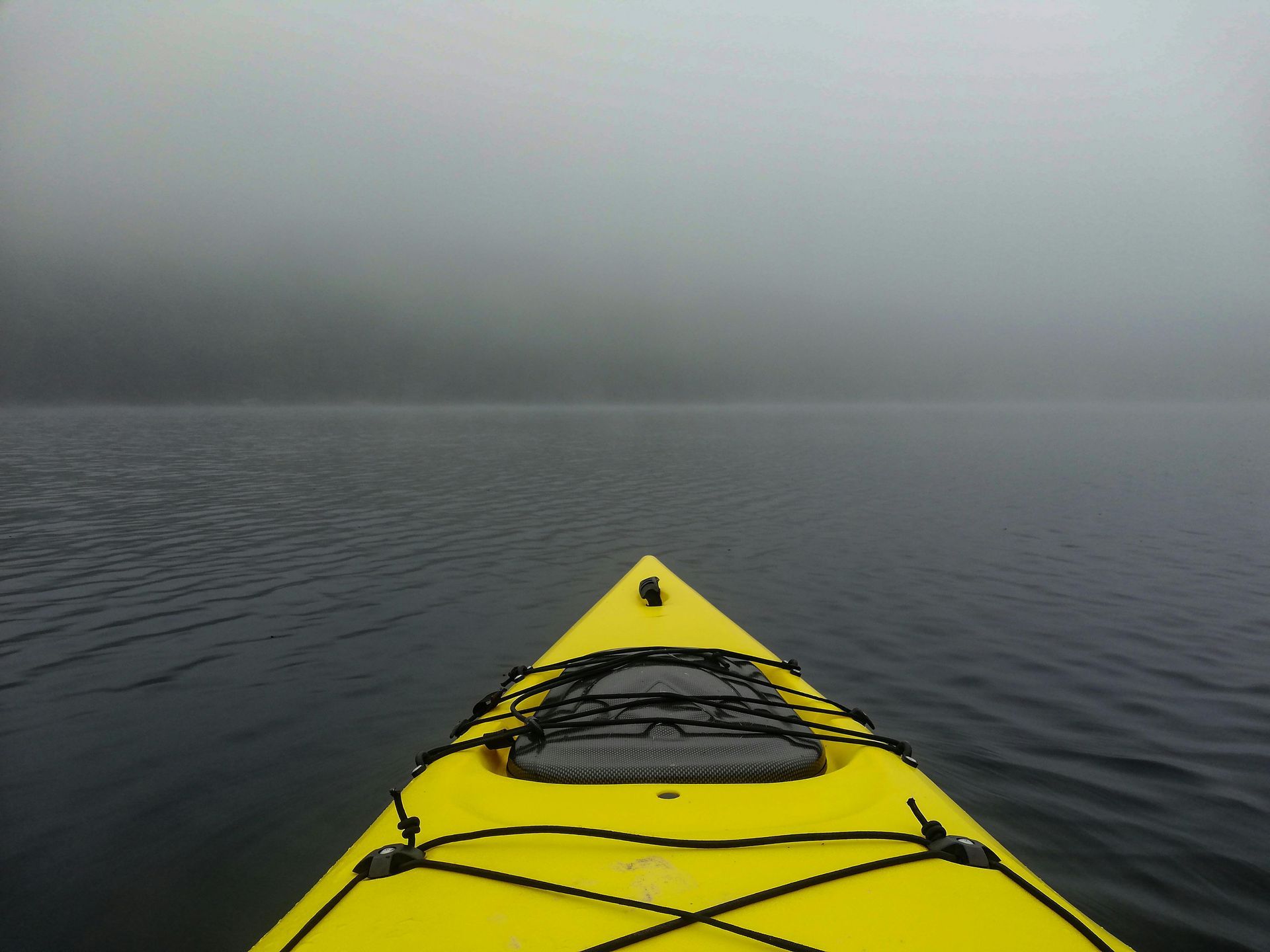 A yellow kayak is floating on a foggy lake