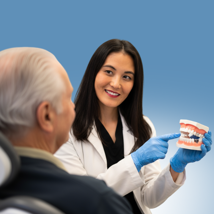 Dentist in white coat talking to a patient in a dental chair; bright office setting.